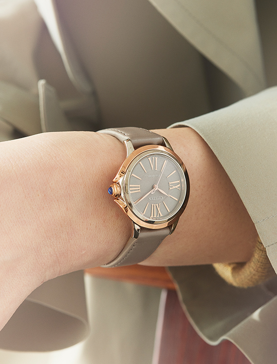 Gros plan d'une montre-bracelet avec bracelet gris et détails dorés au poignet.