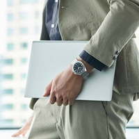 Personne tenant un ordinateur portable, portant une montre et un costume, près d'une fenêtre.