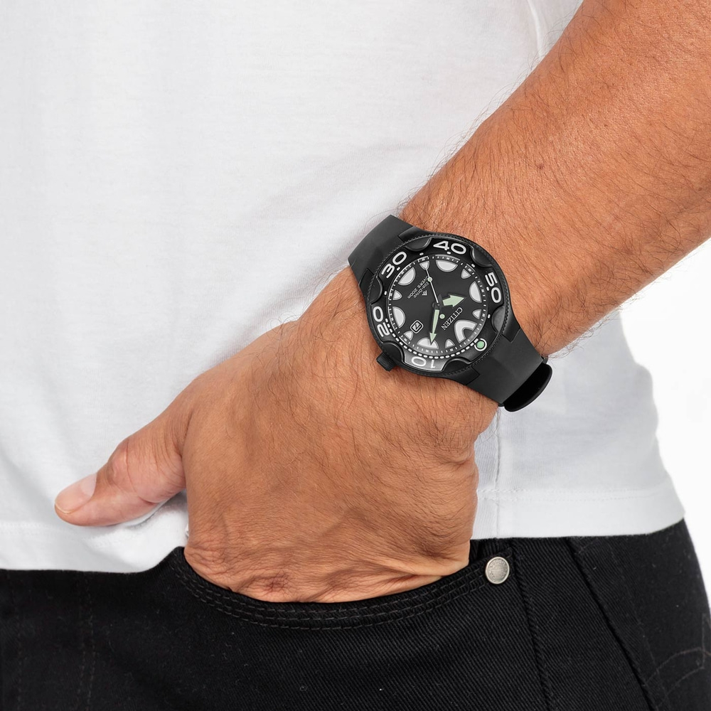Homme portant une montre noire, un t-shirt blanc et un jean noir, la main dans sa poche.