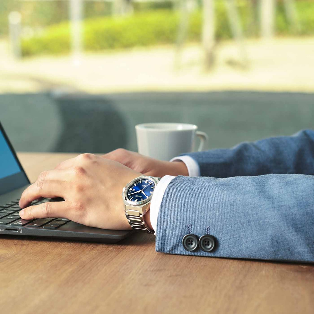Homme portant une montre, tapant sur un ordinateur portable, avec une tasse de café.