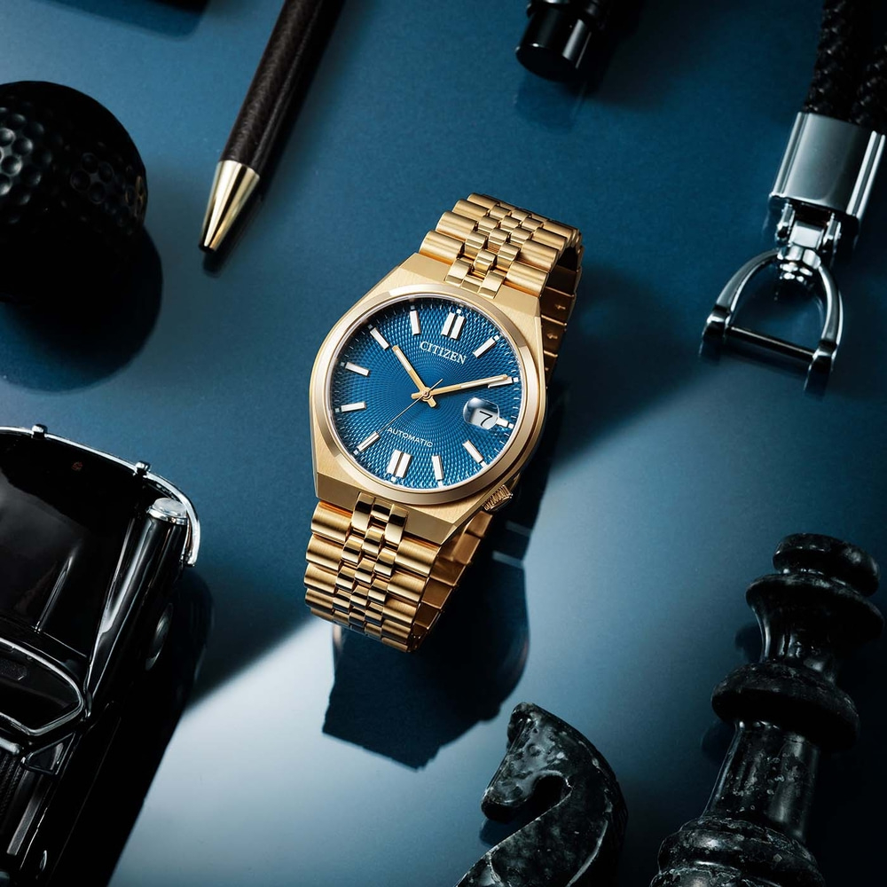 Montre dorée avec cadran bleu, entourée d'accessoires sur fond bleu.