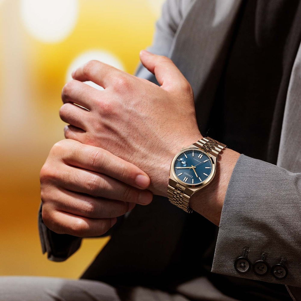 Homme portant une montre dorée avec un cadran bleu et un costume gris.