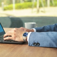 Homme portant une montre, tapant sur un ordinateur portable, avec une tasse de café.