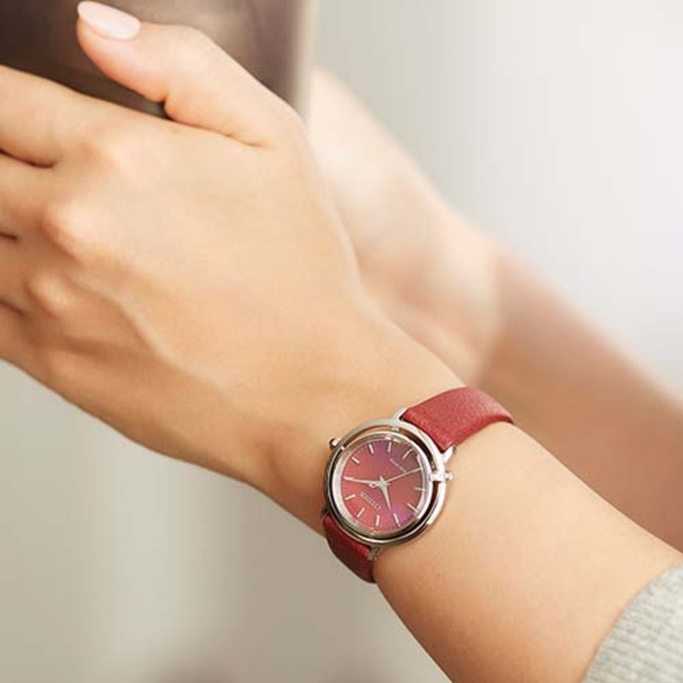 Un poignet de femme avec une montre rouge. La montre a un bracelet rouge et un boîtier argenté.