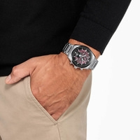 Homme portant une montre, main dans la poche, pull noir, pantalon beige