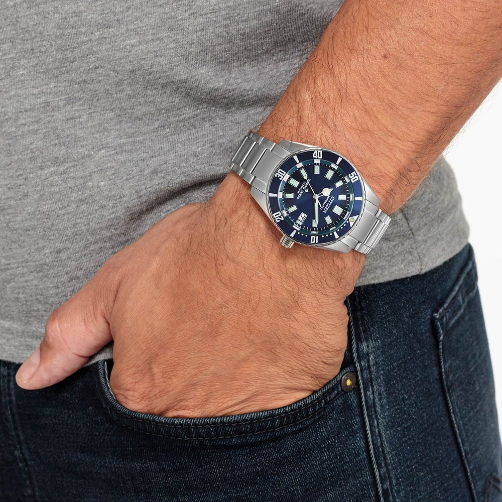 Homme portant une montre Citizen, cadran bleu, bracelet en acier inoxydable, jean et chemise grise.