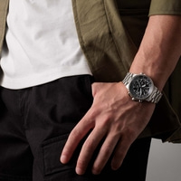 Homme portant une montre, pantalon noir, chemise blanche et veste verte.