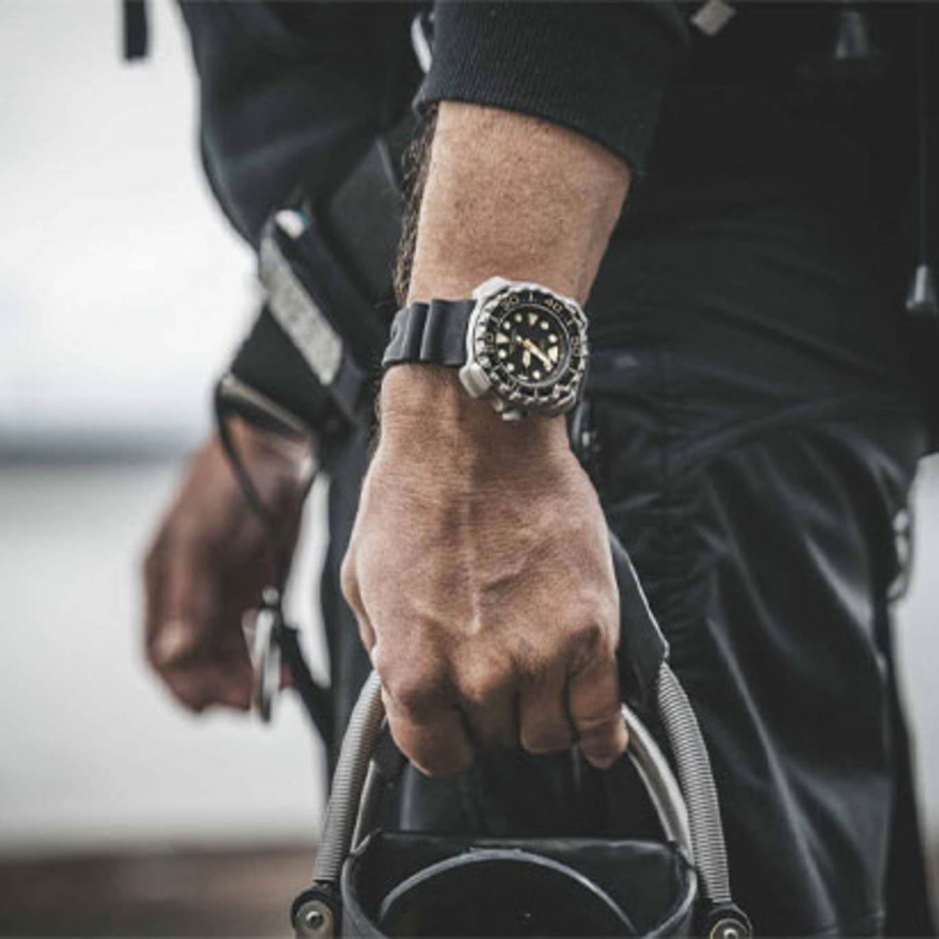 Homme portant une montre, tenant un équipement, gros plan, tenue noire, extérieur