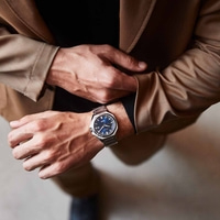 Homme portant une montre, mains sur une veste marron, gros plan