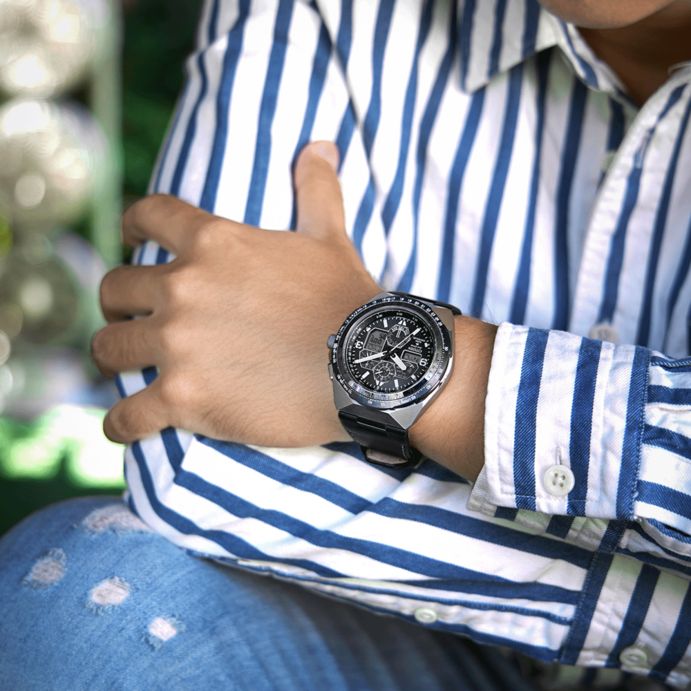 Homme portant une montre, chemise rayée bleue et blanche, et jean déchiré.
